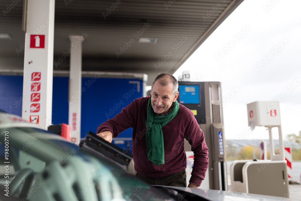 Senior man washing car windscreen at gas station Senior man washing car windscreen at gas station