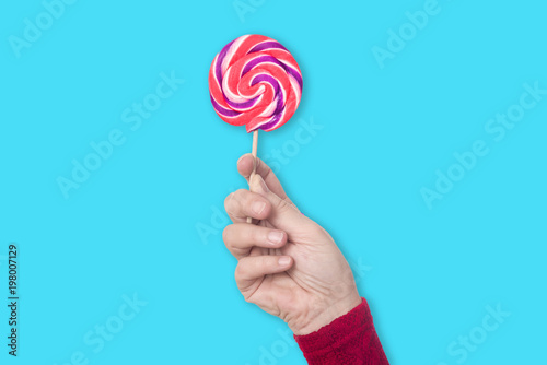 Right female hand holds colorful lollipop upright isolated on pastel light blue background - concept lollipop sweets sugar health tast food kids family fun