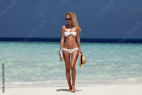 Summer girl model with tanned sexy body. Posing in the white swimsuit on the beach of the tropical island
