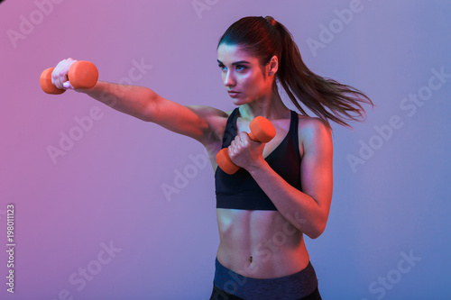 Serious young sports woman make exercises with dumbbells