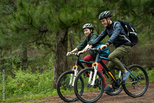 Side view of young Asian couple wearing helmets while practicing cross-country cycling