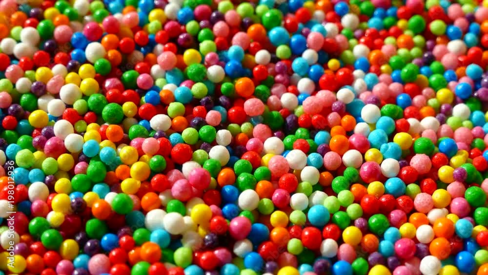 A multi-colored dragee spins on a plate. Multicolored balls. All the colors of the rainbow. Colored easter dragees. Red blue green yellow white white orange. A multi-colored dragee spins on a plate. Multicolored balls. All the colors of the rainbow. Colored easter dragees. Red blue green yellow white white orange.