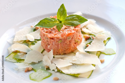 Salmon Tartar with sliced cheese, pesto sauce pine nuts and basil on white plate. raw red fish meat dish, shallow depth of field