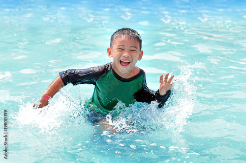 happy asian boy in green and black shirt swiming in clear blue water pool © kittisak
