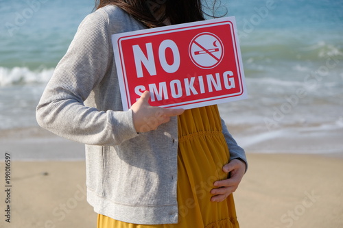 海岸で禁煙プレートを持つ妊婦  Pregnant woman who has a no smoking plate at a coast photo