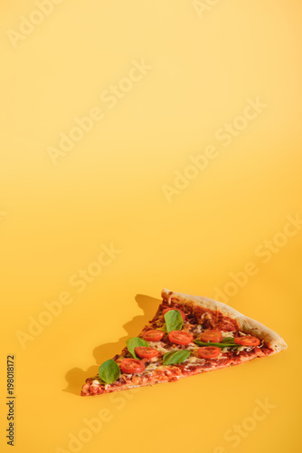 close up view of piece of pizza with cherry tomatoes and basil on orange backdrop