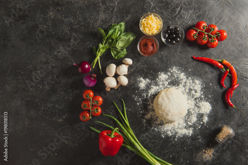 flat lay with raw dough and fresh ingredients for pizza on dark surface