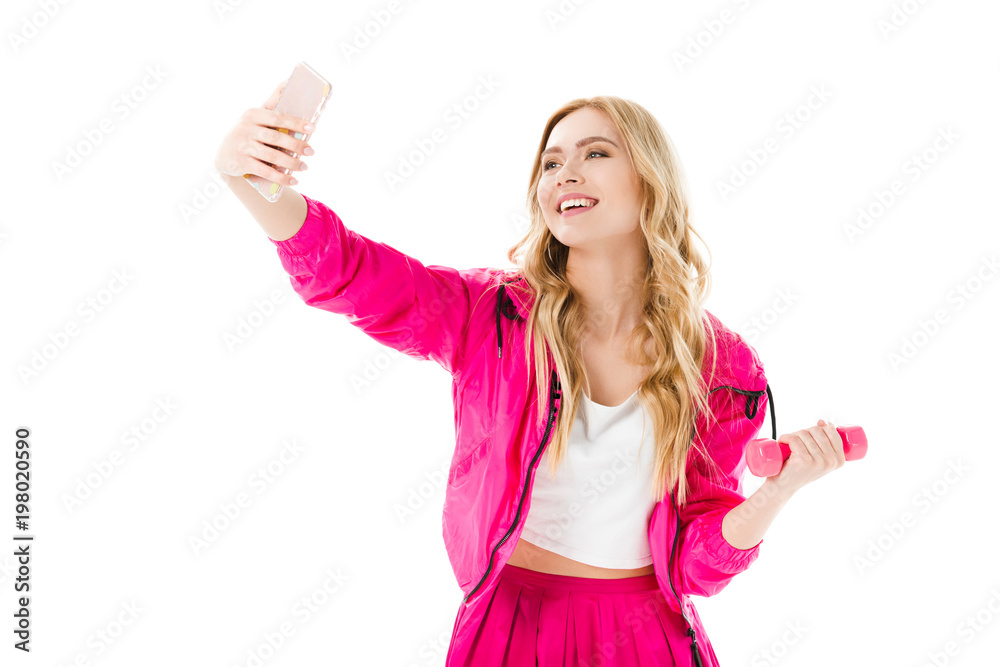 Blonde woman in pink clothes holding dumbbell and taking selfie isolated on white Blonde woman in pink clothes holding dumbbell and taking selfie isolated on white