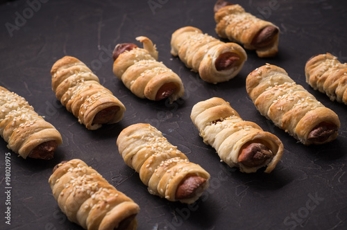 homemade pastries: several sausages in a dough on a black background.