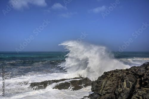 Eine Welle bricht sich an einer Klippe mit empor schießender Gischt.
