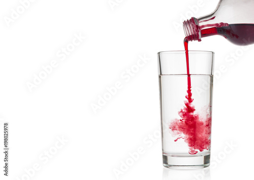 Cranberry syrup pouring into water glass on white background photo