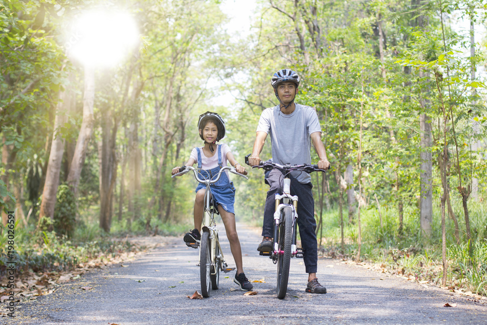 Happy father and daughter cycling in the park, togetherness relaxation concept Happy father and daughter cycling in the park, togetherness relaxation concept