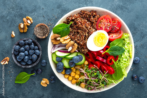 Buddha bowl dinner with boiled egg, chickpea, fresh tomato, sweet pepper, cucumber, savoy cabbage, red onion, green sprouts, spinach leaves, blueberry, walnuts, chia and quinoa