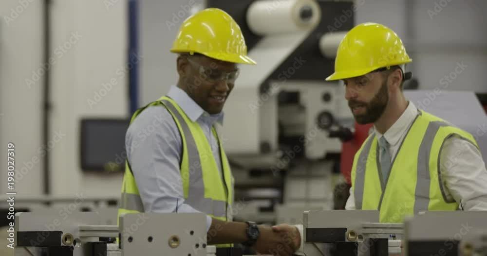 A manager and his foreman shake hands in a production factory. In slow motion