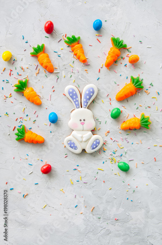 Easter bunny cookies and carrot chewing marmalade with candies on a white stone background. Top view and copy space.