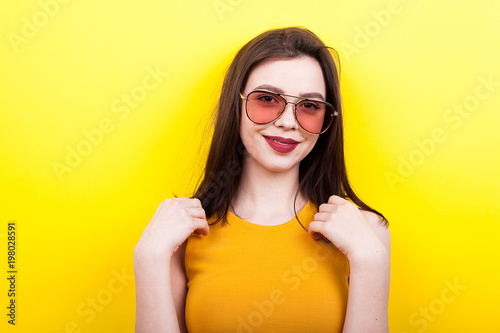 Smiling woman wearing sunglasses on yellow background