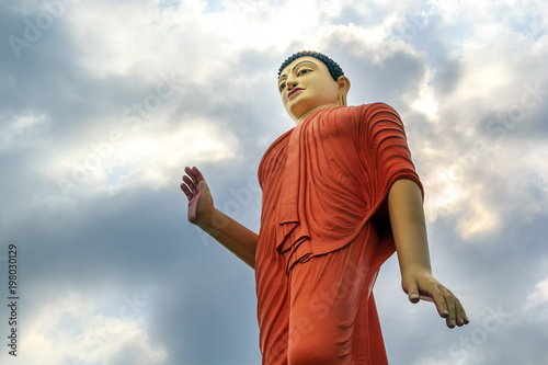 large statue of Buddha rises above the city against a sky with clouds