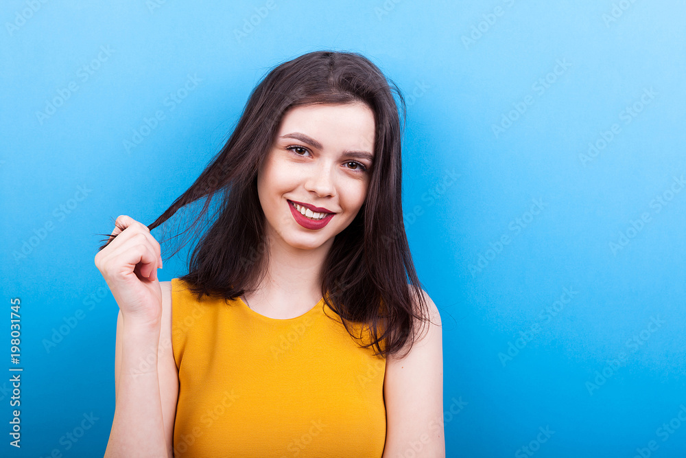 Fototapeta premium Smilng woman playing with her hair on blue background