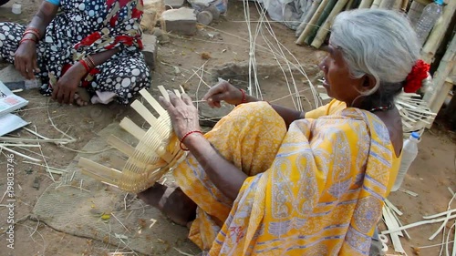 Indian elder lady on yellow saree sitting on the ground making bamboo baskets on the street in Mysore, Karnataka, India. Hard work, humble, poor old rural village woman blue collar job concept