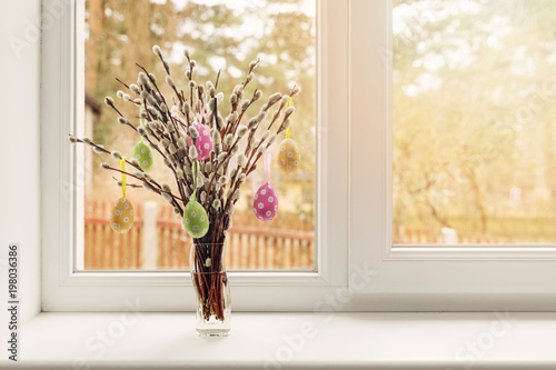 easter decoration - vase with colorful eggs hanging in pussy willow branches on window sill