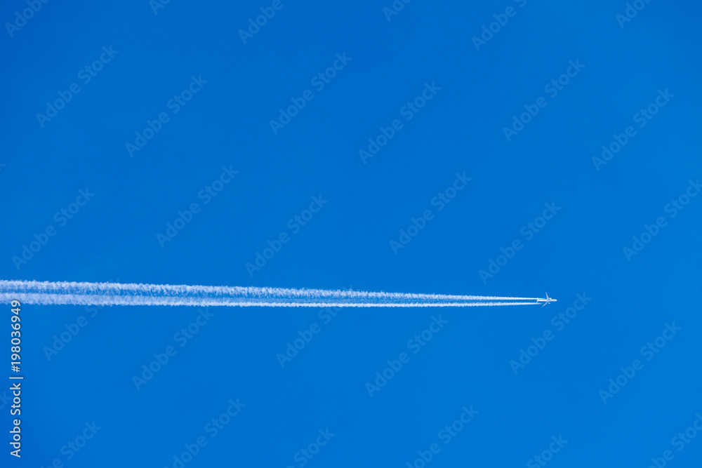 Condensation trace highlighted by the setting sun behind a twin-engine turbojet passenger plane in the March sky