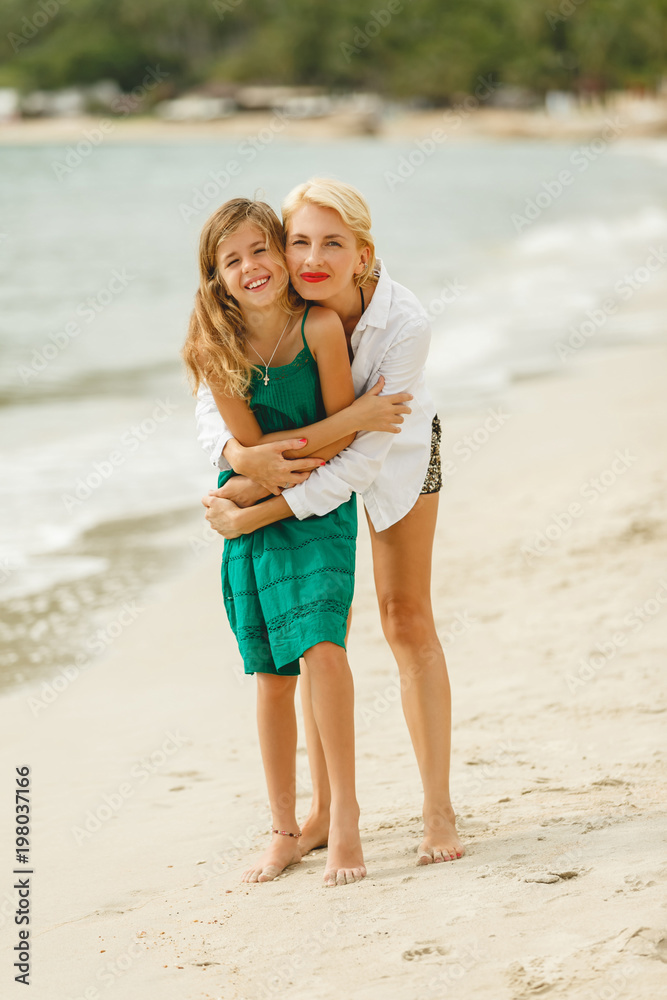 mother and little daughter embracing on beach looking at camera mother and little daughter embracing on beach looking at camera