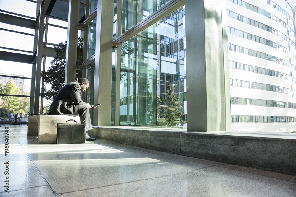 © Mint Images - Business man sitting in waiting area of large open lobby