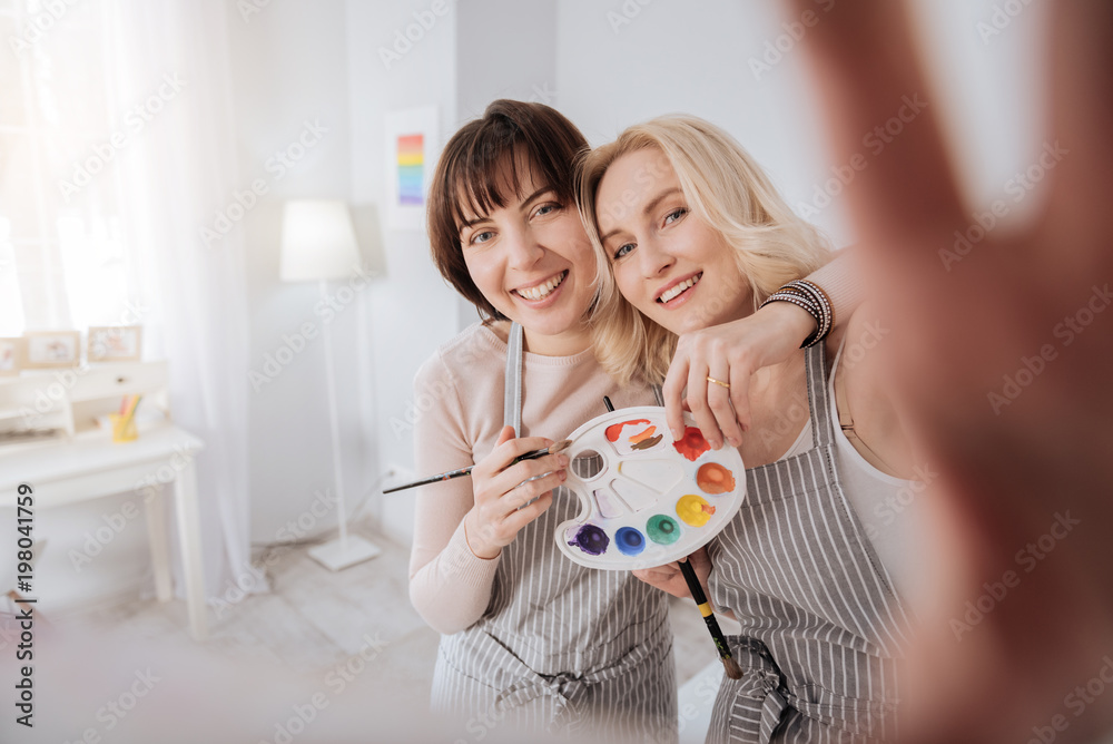 This is art. Positive creative young woman standing together with her girlfriend and holding a camera while taking a photo This is art. Positive creative young woman standing together with her girlfriend and holding a camera while taking a photo