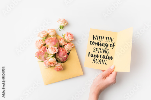 hand holding paper with spring quote beside pink flowers in envelope isolated on white