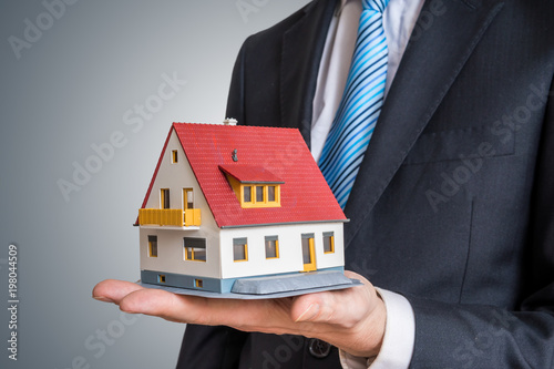 Real estate agent is holding small house in hand.