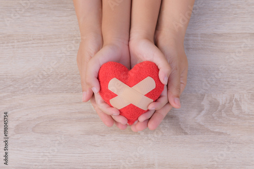 Health care, love, organ donation, family insurance and CSR concept. adult and child hands holding handmade red heart on wooden background. 