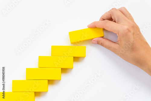 Concept of building success foundation. Women hand put red wooden block on yellow wooden blocks in the shape of a staircase