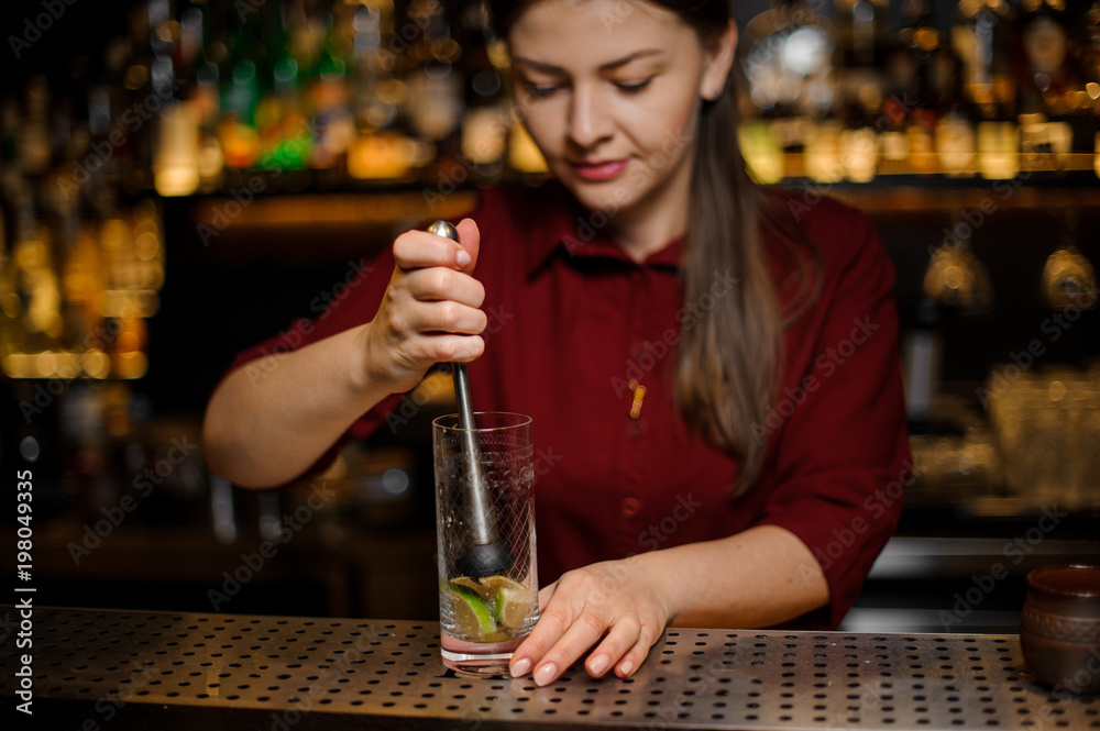 Female bartender pressing down a cane sugar with lime in a glass
