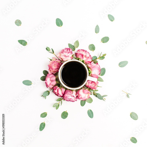 Cup of coffee in frame of pink rose flower buds and eucalyptus branches on white background. Flat lay, top view.