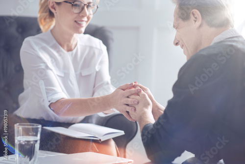 Professional therapist. Pleasant sympathetic female psychologist smiling and holding the hands of her patient while supporting hi 