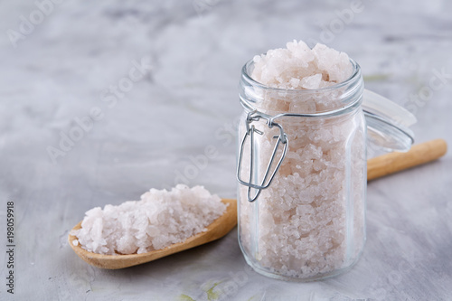 Spa concept. Bath salt pouring out of glass jar on texrured background, close-up, selective focus photo
