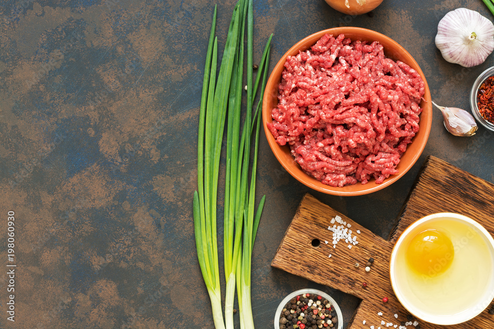 Naklejka premium Ground beef. Ingredients for making cutlets, meatballs - ground beef, raw egg, spices, green onion on dark rustic background. Top view, copy space.