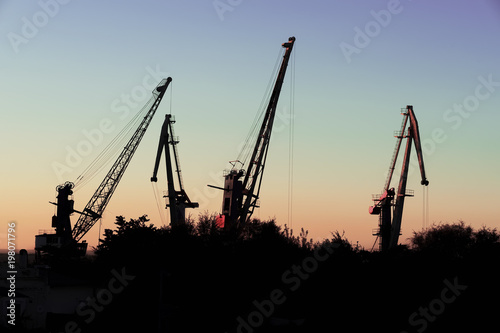 Silhouette of of cargo cranes. Port wharf landscape. Bright sunset, bright sky. Evening sea, river dock