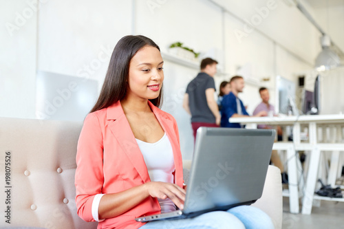 business, education, technology and people concept - happy young african american woman with laptop computer working at office