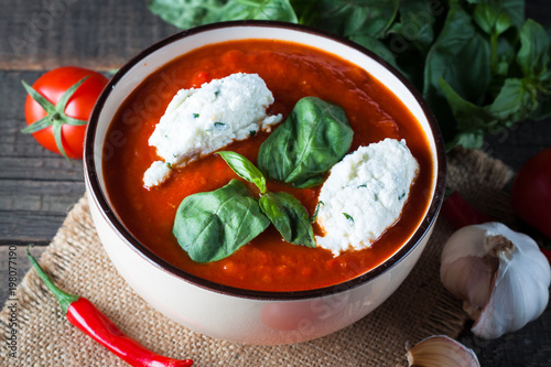 Fotografie Chili tomato soup with sour cream sauce, cottage cheese, basil and red hot peppers on wooden background