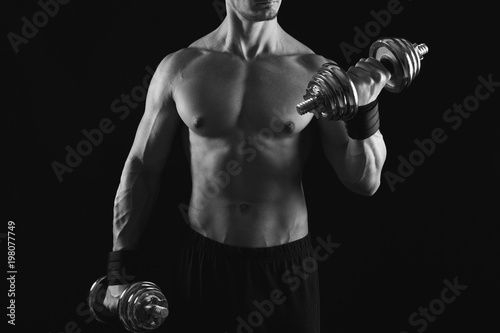 Strong athletic man with dumbbell showes naked muscular body