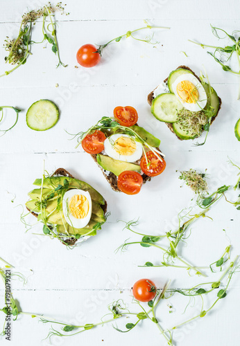Tasty sandwiches with egg, avocado and vegetables on wooden white rustic background