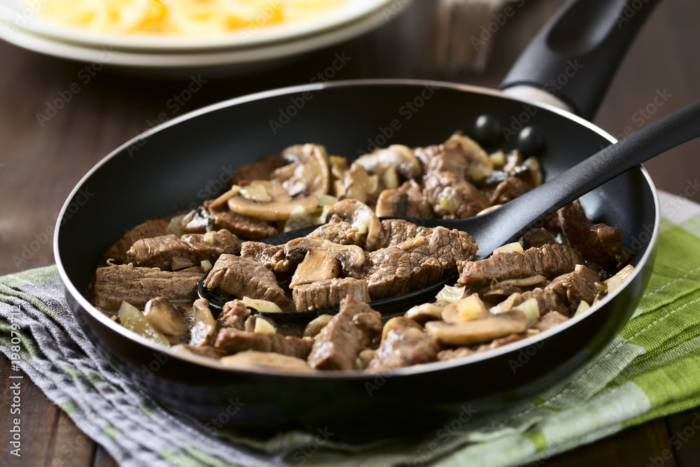 Beef Stroganoff in frying pan, a dish made of pieces of beef, mushroom and onion in cream sauce, photographed with natural light (Selective Focus, Focus in the middle of the dish on the spoon) Beef Stroganoff in frying pan, a dish made of pieces of beef, mushroom and onion in cream sauce, photographed with natural light (Selective Focus, Focus in the middle of the dish on the spoon)