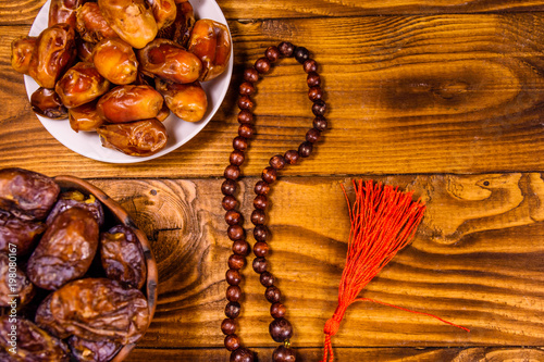 Date fruits and rosary on wooden table. Top view