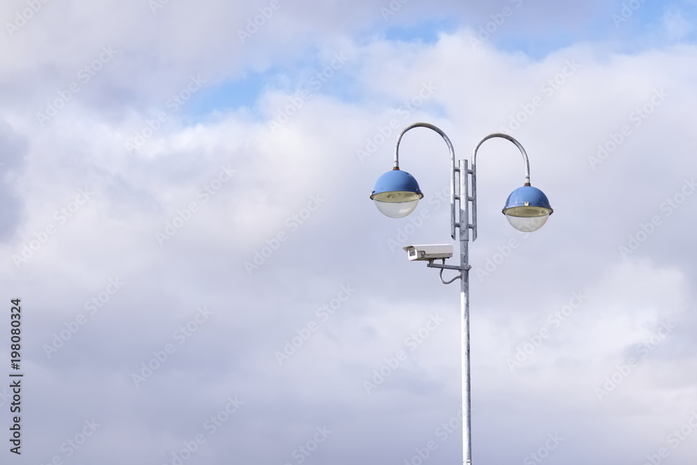 CCTV camera on post in sky blue clouds background and two lights at public office workspace for security and protection CCTV camera on post in sky blue clouds background and two lights at public office workspace for security and protection
