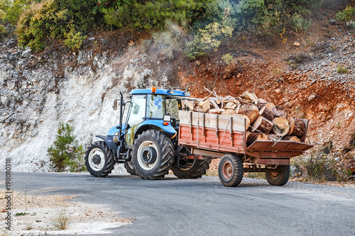 Tractor with wooden logs and chunks on an asphalt road in mountains photo