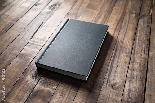Blank black hardcover book on vintage wood table background.