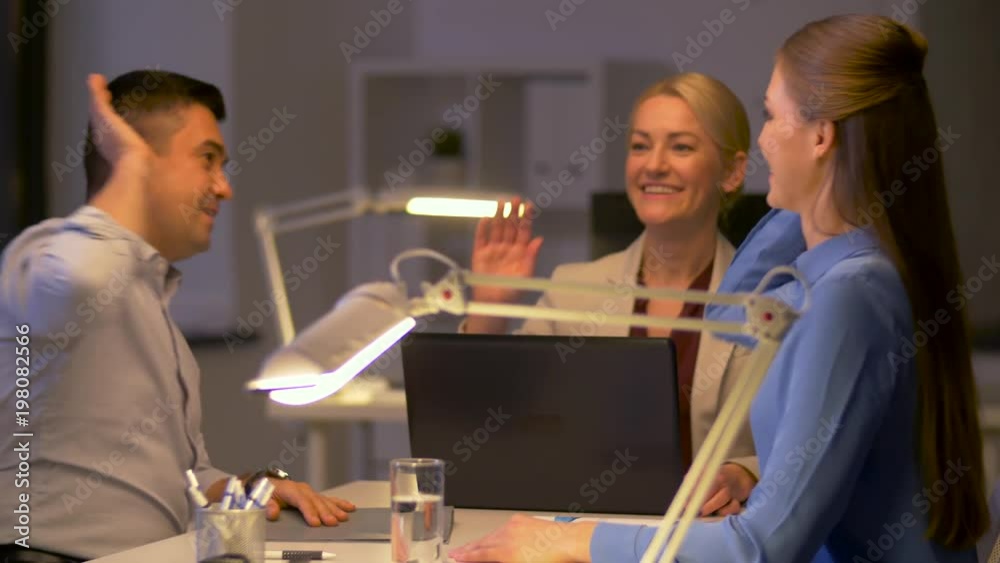 business, deadline and success concept - happy team with papers and laptop computer working late at night office