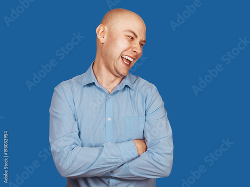 Young bald laughing guy looking aside and crossed arms. Isolated on blue background. photo