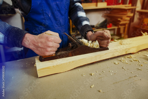 The woodworker keeps in the hands of the plane, which stands on a timber bar and is ready for work. Scraping the bar photo